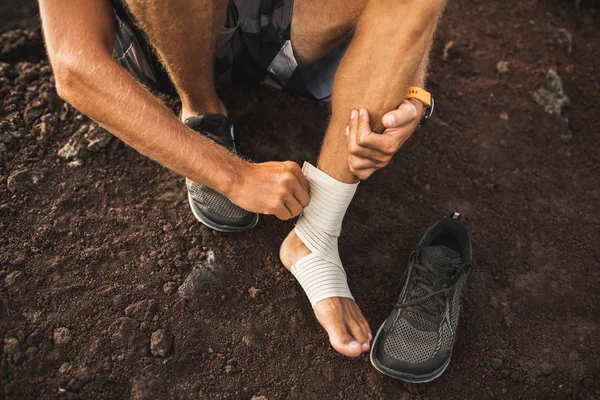 Uomo che bendava la caviglia ferita. Gamba lesione durante la corsa all'aperto . — Foto Stock