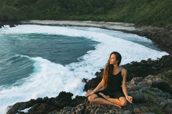 Молодая женщина практикует йогу в позе лотоса на закате с красивым — стоковое фото
