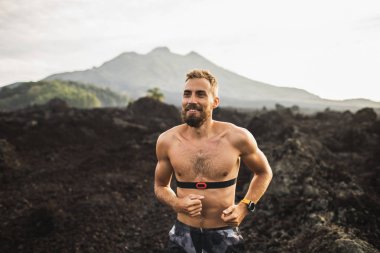 Sakallı genç mutlu adam dışarıda koşuyor ve gülümsüyor. Üstsüz