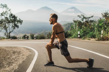 Koşucu yolda koşmadan önce lunges yapıyor ve ısınma. S