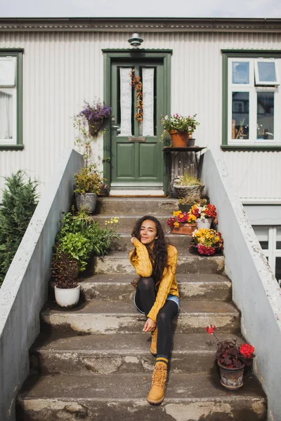 Молодая счастливая женщина в оранжевом свитере и ботинках сидит на лестнице — стоковое фото