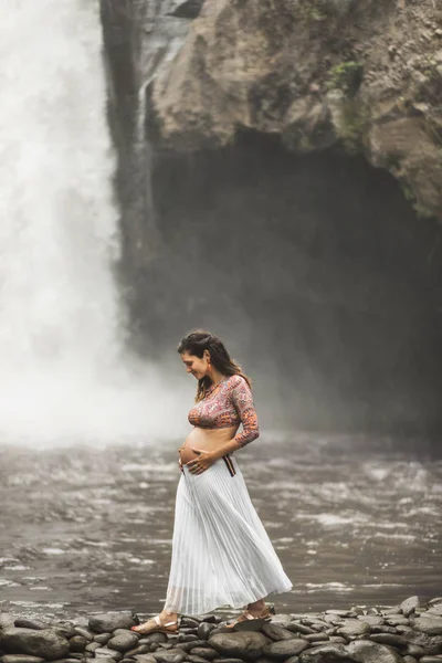 Νεαρή αυθεντική έγκυος γυναίκα κοντά σε εκπληκτικό καταρράκτη. Ν — Φωτογραφία Αρχείου