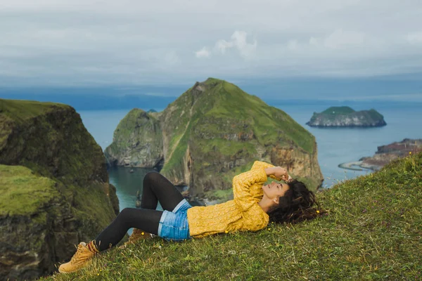 穿着橙色毛衣的快乐的年轻女人躺在青草山上 — 图库照片