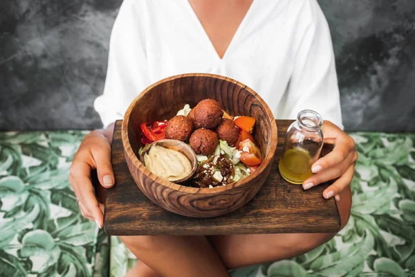 Vrouw die falafelballen, hummus en verse salade in houten strik eet — Stockfoto