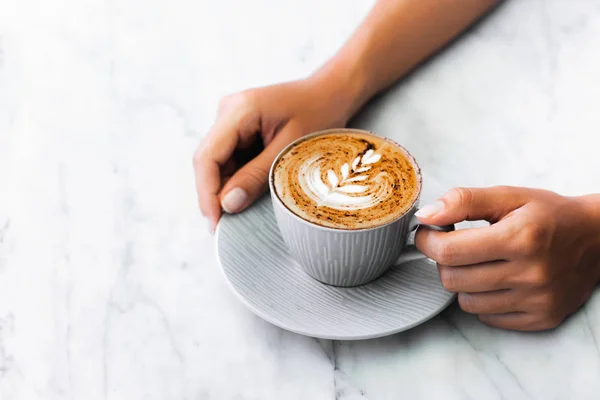 Kupa friss kávé cappuccino női kézben fehér márvány ta — Stock Fotó