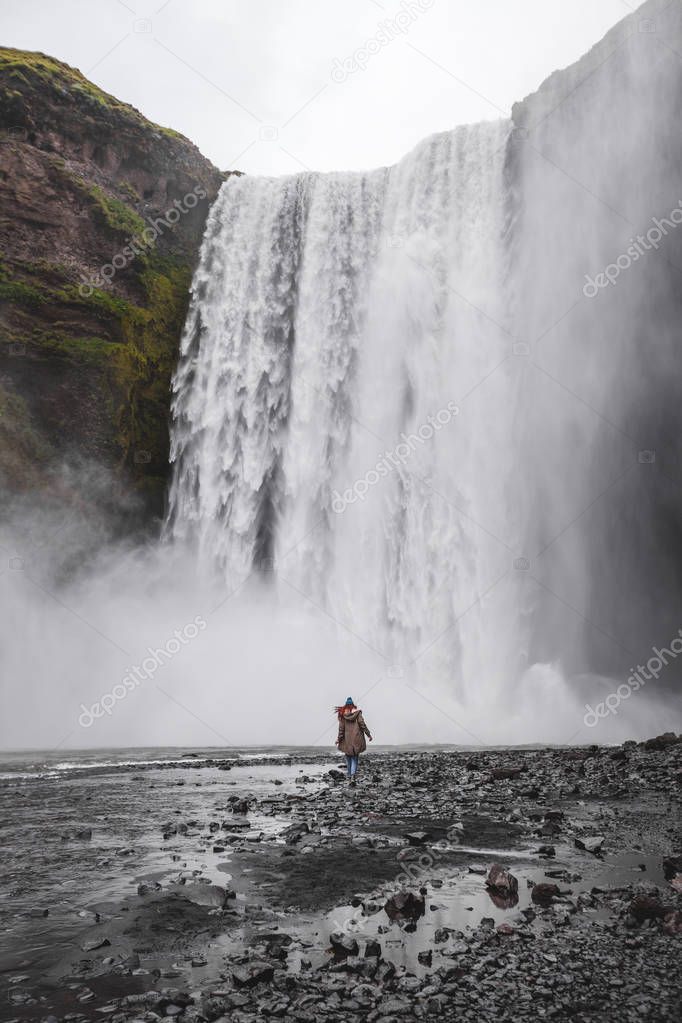 Woman walking to Skogafoss Iceland famous waterfall. Powerful st