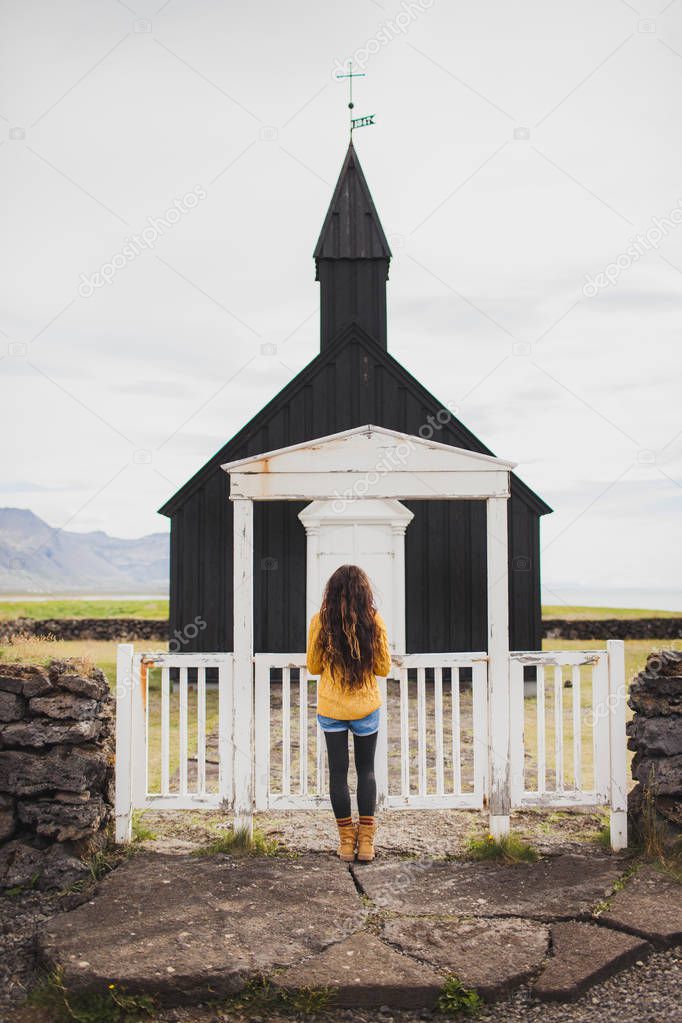 Woman looking on Famous black church of Budir at Snaefellsnes pe