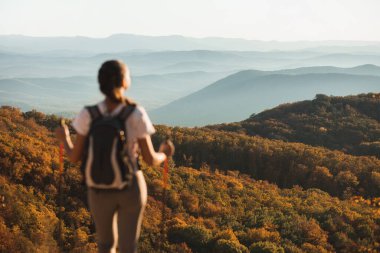 Sonbahar katmanlı dağ manzarasından hoşlanan bir kadın. Turuncu sonbahar ormanı ve ufuktaki mavi tepeler. Doğadaki güzellik, arka plandaki boş yer..