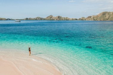 Tropik tatil konsepti. Muhteşem dağ manzaralı ve turkuaz suyla sahilde eğlenen mutlu kadın. Drone hava görüntüsü.