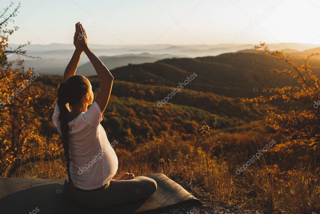 Spiritual and emotional concept of harmony with nature in maternity time. Pregnant woman practicing yoga outdoors on hill at sunset. Amazing autumn mountain view.