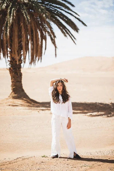 穿着白衬衫和裤子的年轻黑发女人时髦的肖像 背景是棕榈 沙漠和沙丘 生活方式概念 — 图库照片