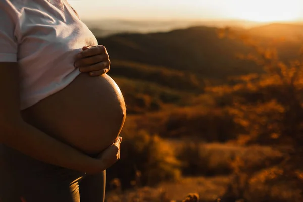 妊娠中の女性の手は戸外で腹を保持します 素晴らしい暖かい日没の光 出産の概念 — ストック写真