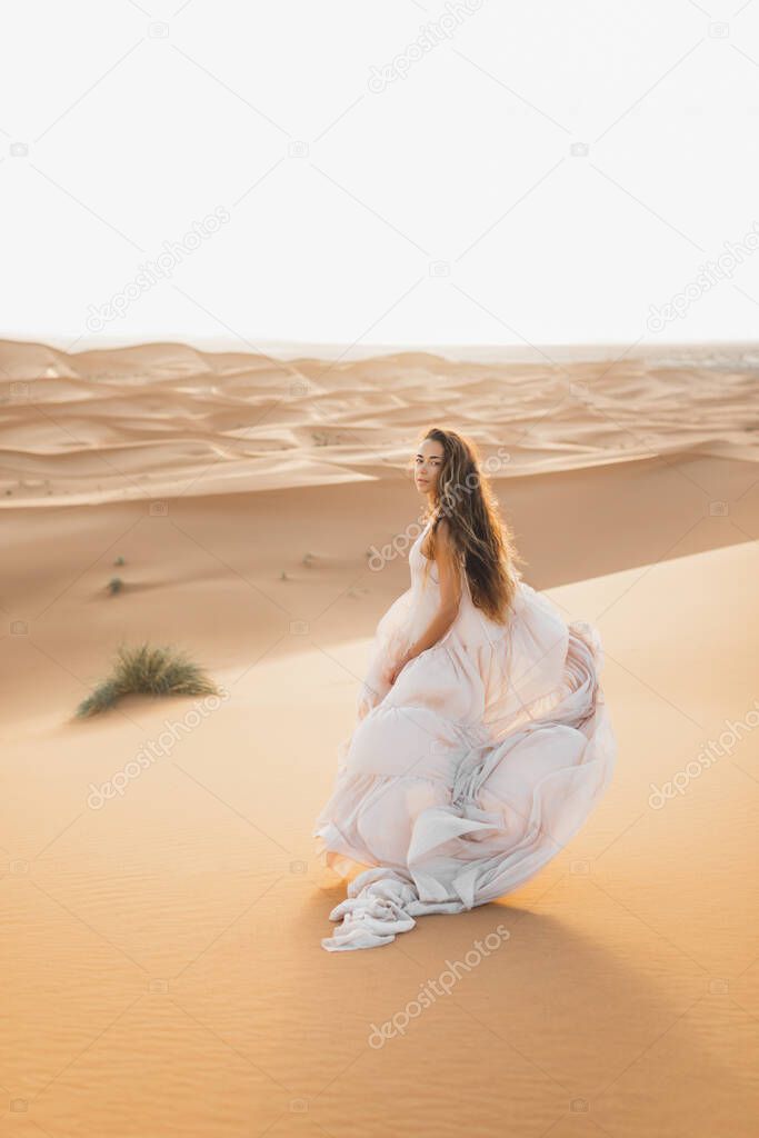 Portrait of bride woman in amazing wedding dress in Sahara desert, Morocco. Warm evening light, beautiful pastel tone, sand dunes on horizon.