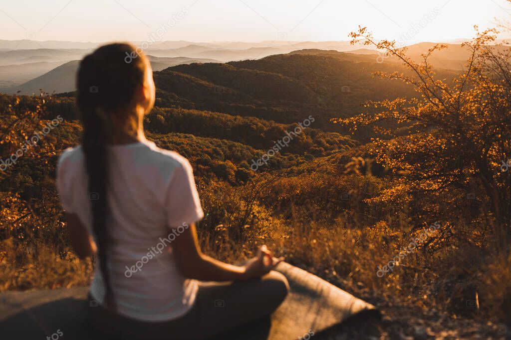 Woman meditating alone on hill with amazing autumn mountain view at sunset. Zen spiritual concept. Praying alone, harmony with nature.