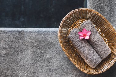 Otel spa 'sında havuz başında hasır sepetin içinde iki gri el havlusu. Dekorasyon olarak pembe frangipani çiçeği. Güzellik tedavisi.