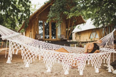 Tropik plajda el yapımı makrome hamakta dinlenen bir kadın. Seyahat, eğlence ve tatil konsepti.