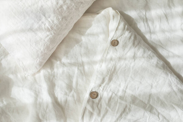 Trendy organic natural linen bedclothes with wooden buttons closeup. Bedding, morning light, bedroom style and design. Rough textile background with wrinkle.