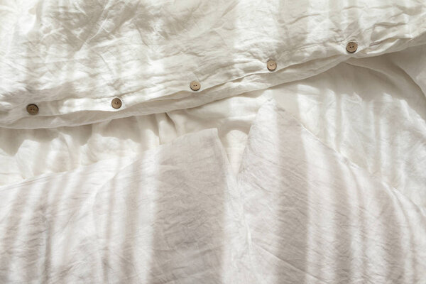 Trendy organic natural linen bedclothes with wooden buttons closeup. Bedding, morning light, bedroom style and design. Rough textile background with wrinkle.