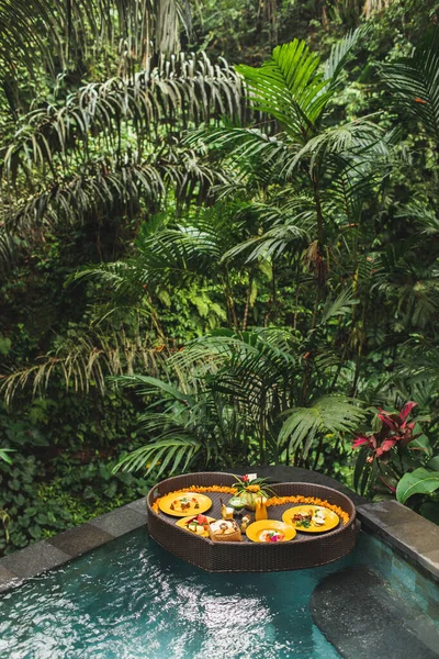 ジャングルスイミングプール 熱帯リゾートで浮動朝食 ハート型の黒い籐のトレイ バレンタインデーや新婚旅行の驚き 上からの眺め エキゾチックな夏の食事 熱帯のビーチライフスタイル — ストック写真