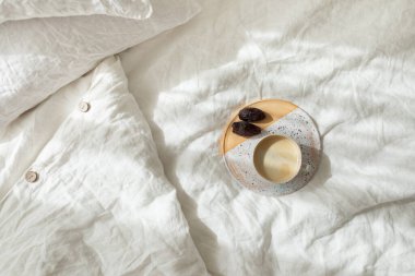 Seramik tepside yatakta bir fincan taze kahve, sabah havası. Pamuklu çarşaf çarşafları. Organik ve doğal keten. Yatak odasının içi rahattır. Güzel ışık.