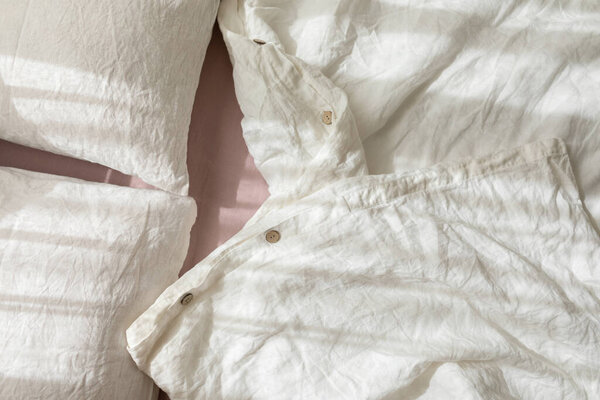 Trendy organic natural linen bedclothes with wooden buttons closeup. Bedding, morning light, bedroom style and design. Rough textile background with wrinkle.
