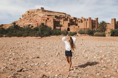Genç kıvırcık kadın doğuda Kasbah Ait-Ben-Haddou 'nun arka planında yürüyor. Fas 'a git, Ouarzazate. Yaz tatilleri, seyahat yaşam tarzı konsepti..