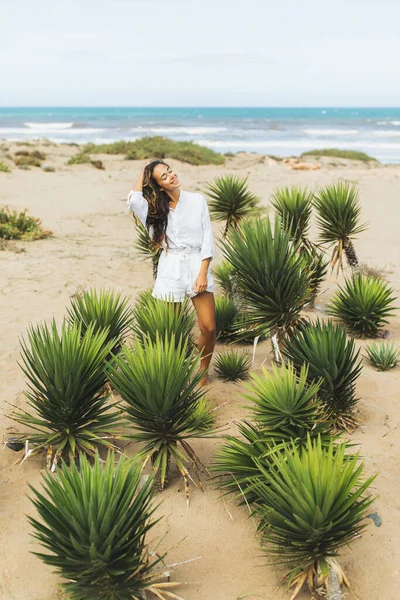 幸せな女性の白いシャツと砂の海のビーチでのショートパンツで笑顔 熱帯緑のサボテンの植物 風の強い日 — ストック写真