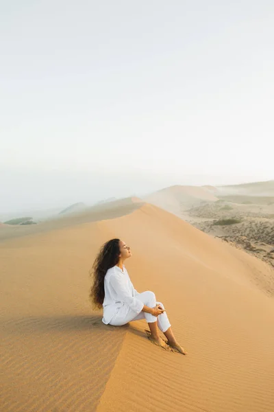 在摩洛哥的撒哈拉沙漠上 穿着白色衣服的美丽的黑发女人在沙丘上悠闲自在地躺着 黎明前的薄雾 与自然和谐相处 — 图库照片