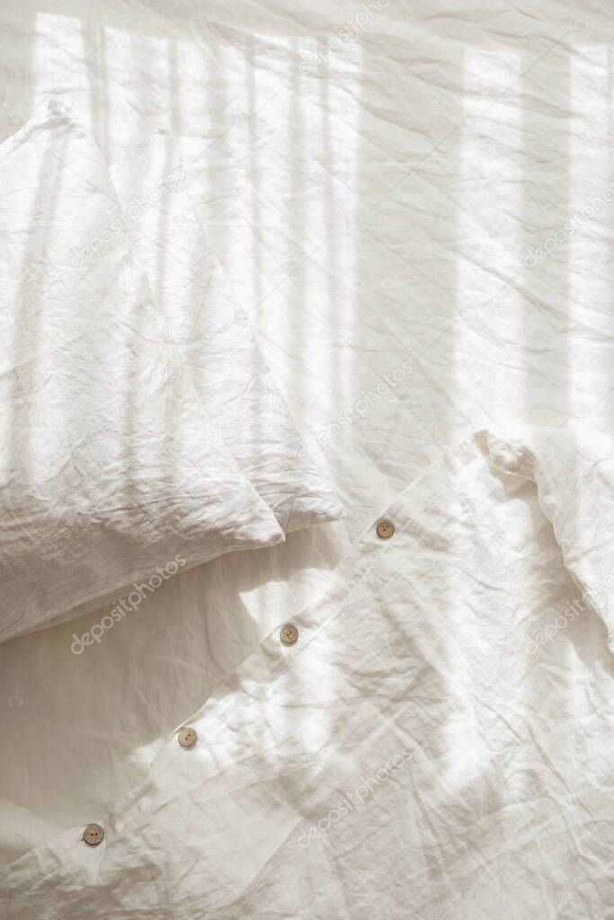 Trendy organic natural linen bedclothes with wooden buttons closeup. Bedding, morning light, bedroom style and design. Rough textile background with wrinkle.