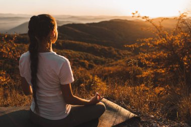 Kadın gün batımında muhteşem sonbahar dağ manzaralı tepede tek başına meditasyon yapıyor. Zen manevi kavramı. Yalnız dua etmek, doğayla uyum içinde olmak..