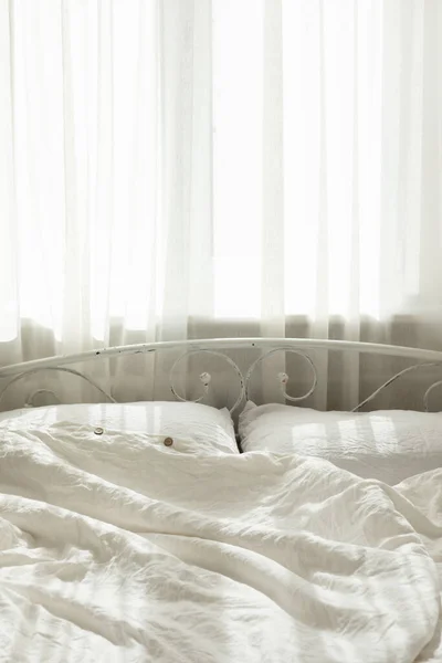 Beautiful morning light in bedroom. Pastel color white bedding. Trendy organic natural linen bedclothes. Cozy home interior.