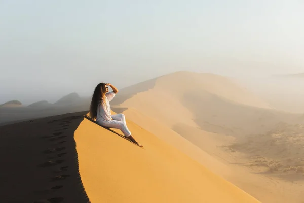 Dream destination, travel and wanderlust concept. Happy woman inspired by fantastic sunrise in Sahara desert sand dunes, Morocco. Mist in morning and warm light.