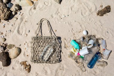 Tek kullanımlık plastik ile yeniden kullanılabilir arasında bir seçim. Sürdürülebilir yaşam tarzı ve konsept. Kumsalda çöp yığını ve cam şişeli hasır çanta. Plastiksiz ve sıfır atık.