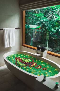 Güzellik tedavisi için tropik çiçeklerle dolu lüks taş küvet, otelde rahatlama. Orman penceresi manzarası. Bali tarzı.