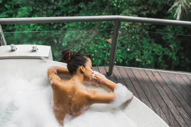 Kadın, orman manzaralı köpükle dolu küvette dinleniyor. Arkadan bak. Güzellik spa tedavisi, boş zaman.