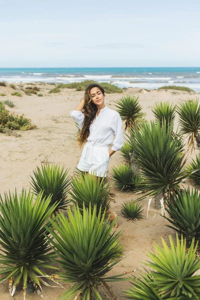 幸せな女性の白いシャツと砂の海のビーチでのショートパンツで笑顔 熱帯緑のサボテンの植物 風の強い日 — ストック写真