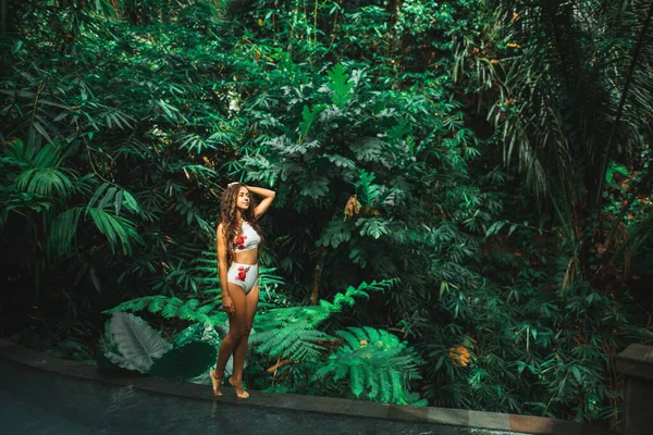 ジャングルの屋外でエッジ高級スイミングプールで白い水着の美しいスリムブルネットの女性 バリ島 — ストック写真