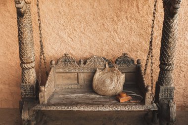 Zincirlere kazınmış güzel ahşap salıncak. Eski fotoğraf makinesi için el yapımı hasır çanta ve deri çanta. Terracotta duvarı.