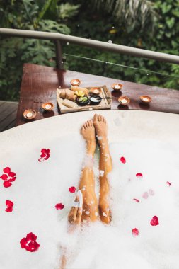 Bacaklarını köpükle yıkayan bir kadın ve doğal lif süngeri kullanıyor. Spa, vücut bakımı, romantik ruh hali..