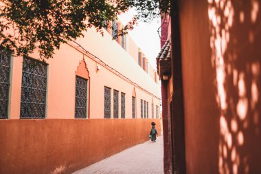 Geleneksel Arap siyah pelerinli ve Marakeş Caddesi 'nde kafasında çanta taşıyan bir kadın. Arkadan bak. Kırmızı şehir, terracotta renk arkaplanı.