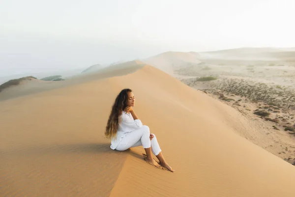 モロッコのサハラ砂漠で砂丘の上でリラックス白い服を着た美しいブルネットの女性 日の出前の朝の霧 自然との調和 — ストック写真