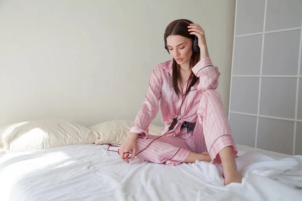 Morena mujer en pijama escuchando música se encuentra en la cama —  Fotos de Stock