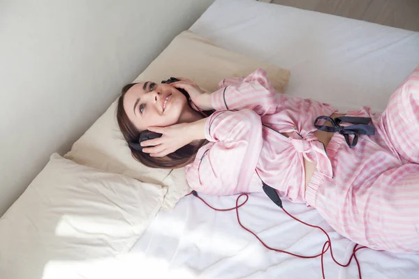Mulher morena de pijama ouvindo música fica na cama — Fotografia de Stock