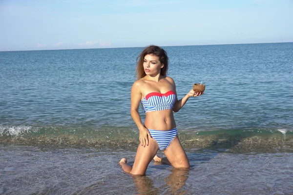 Een vrouw in een badpak met een cocktail op het strand zee — Stockfoto