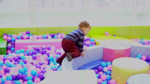 Маленький мальчик играет на детской площадке с мячами — стоковое видео