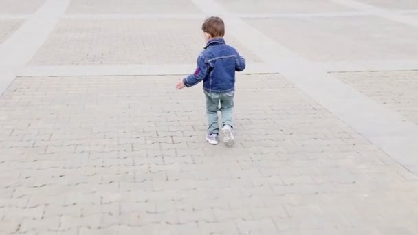 Een kleine jongen die draait rond de weg loopt — Stockvideo