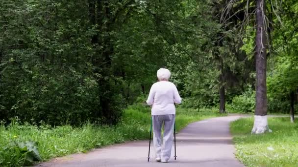 Бабушка гуляет в парке с палками для скандинавских прогулок на пенсию — стоковое видео