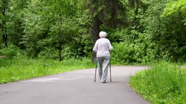Бабушка гуляет в парке с палками для скандинавских прогулок на пенсию — стоковое видео