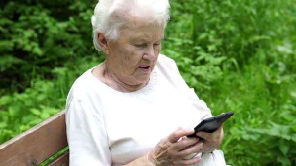 Vieja abuelita mira en el teléfono inteligente Internet — Vídeos de Stock