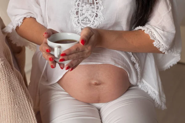 Der Magen einer schwangeren Frau hält eine Tasse Tee oder Kaffee — Stockfoto